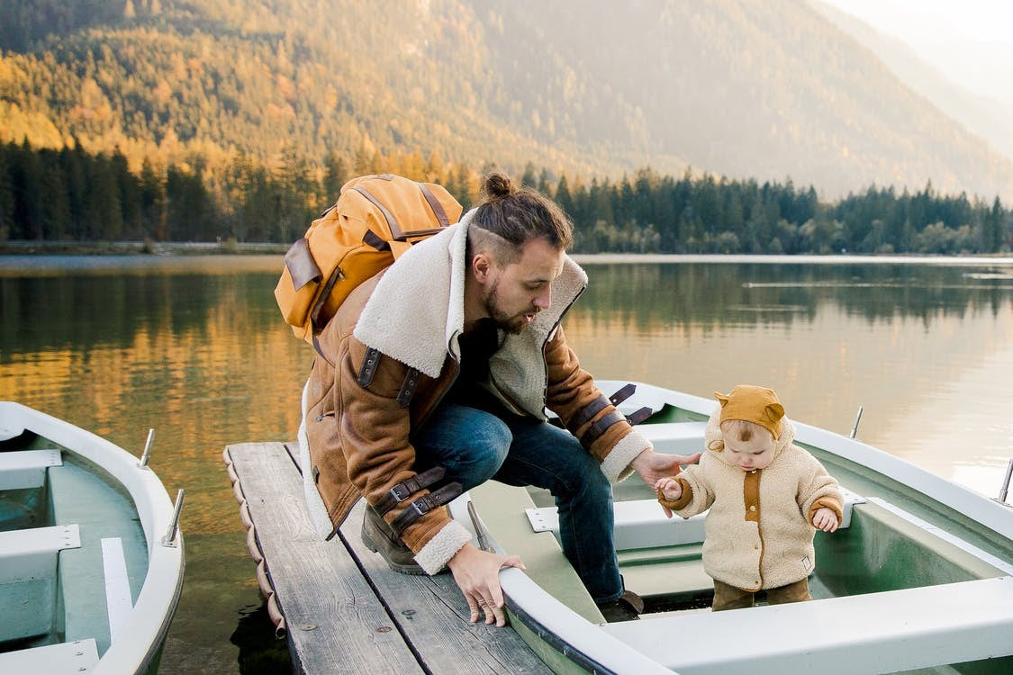 A Baby with Dad standing in a boat near lakes in the mountain